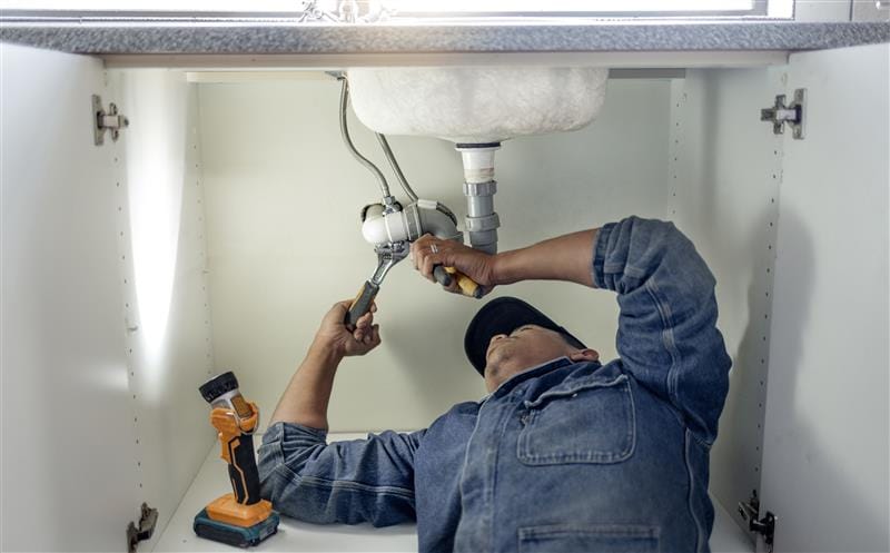Plumber repairing pipes beneath a bathroom sink in Folsom